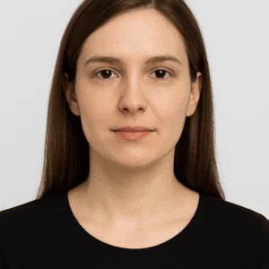 Clear portrait of a young woman with brown hair and neutral expression, minimalist background.