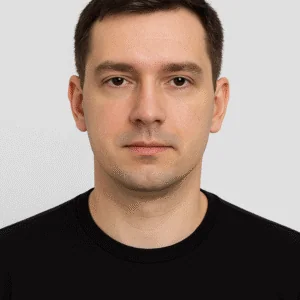 Male portrait, clean-shaven man with brown hair, neutral expression, grey background, casual black shirt, professional headshot.