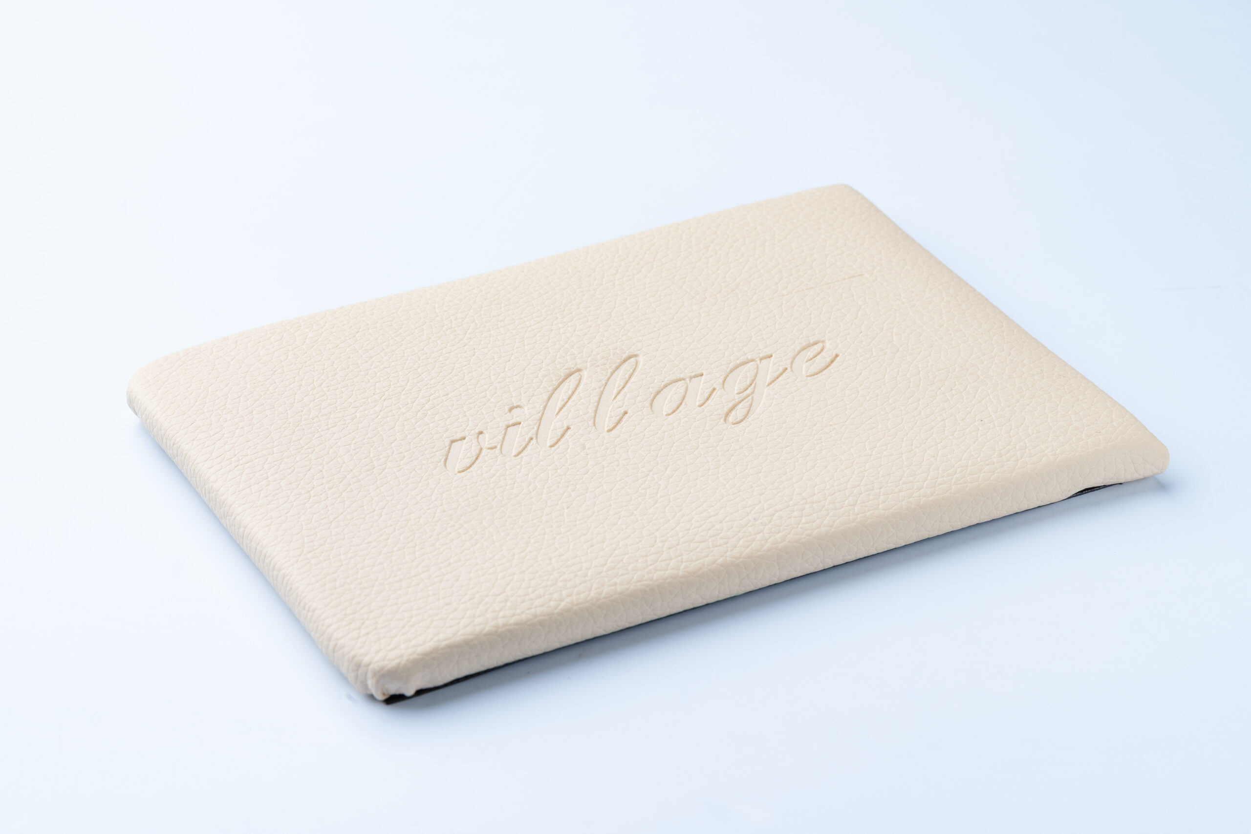 Cream-coloured textured notebook with 'village' embossed on cover on light blue background.