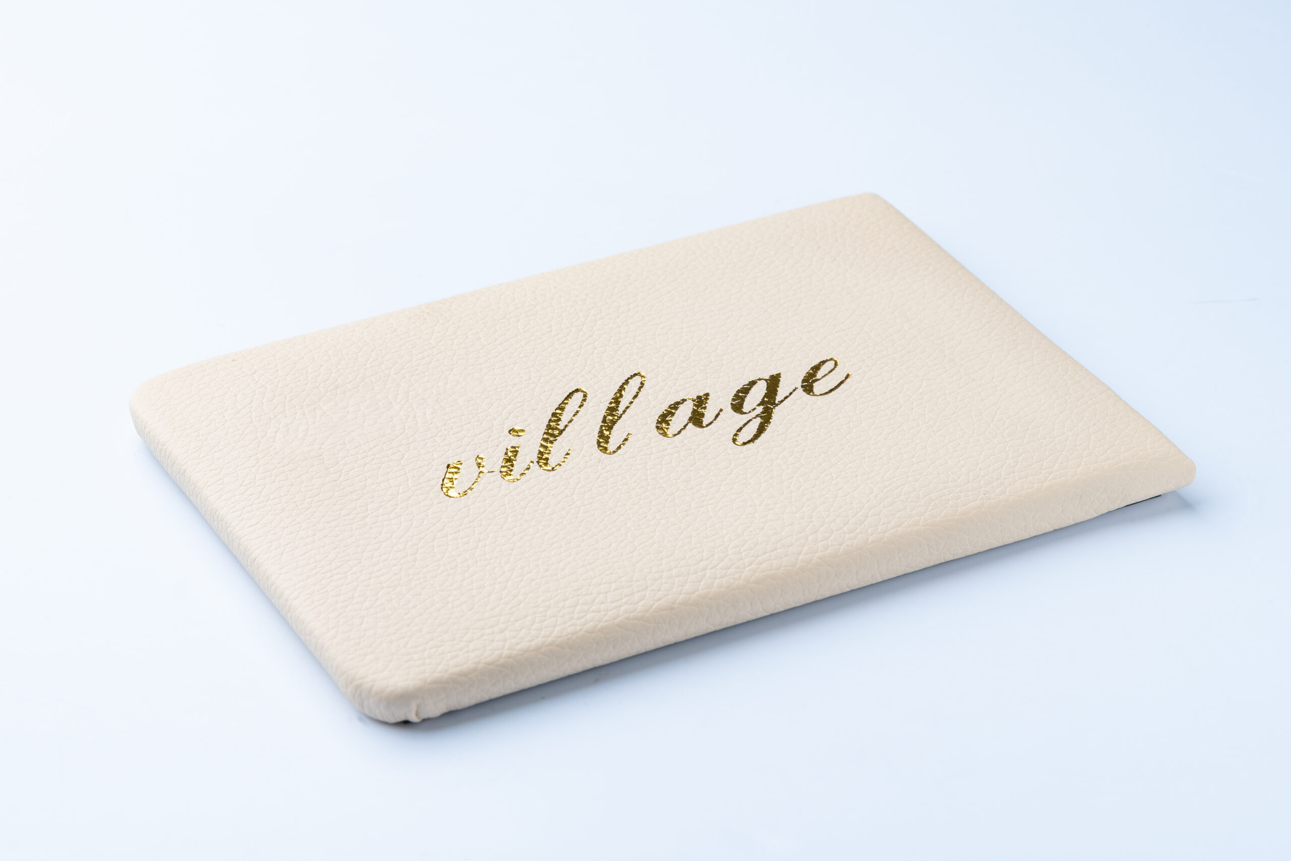 Cream textured notebook with 'village' written in gold script on cover.