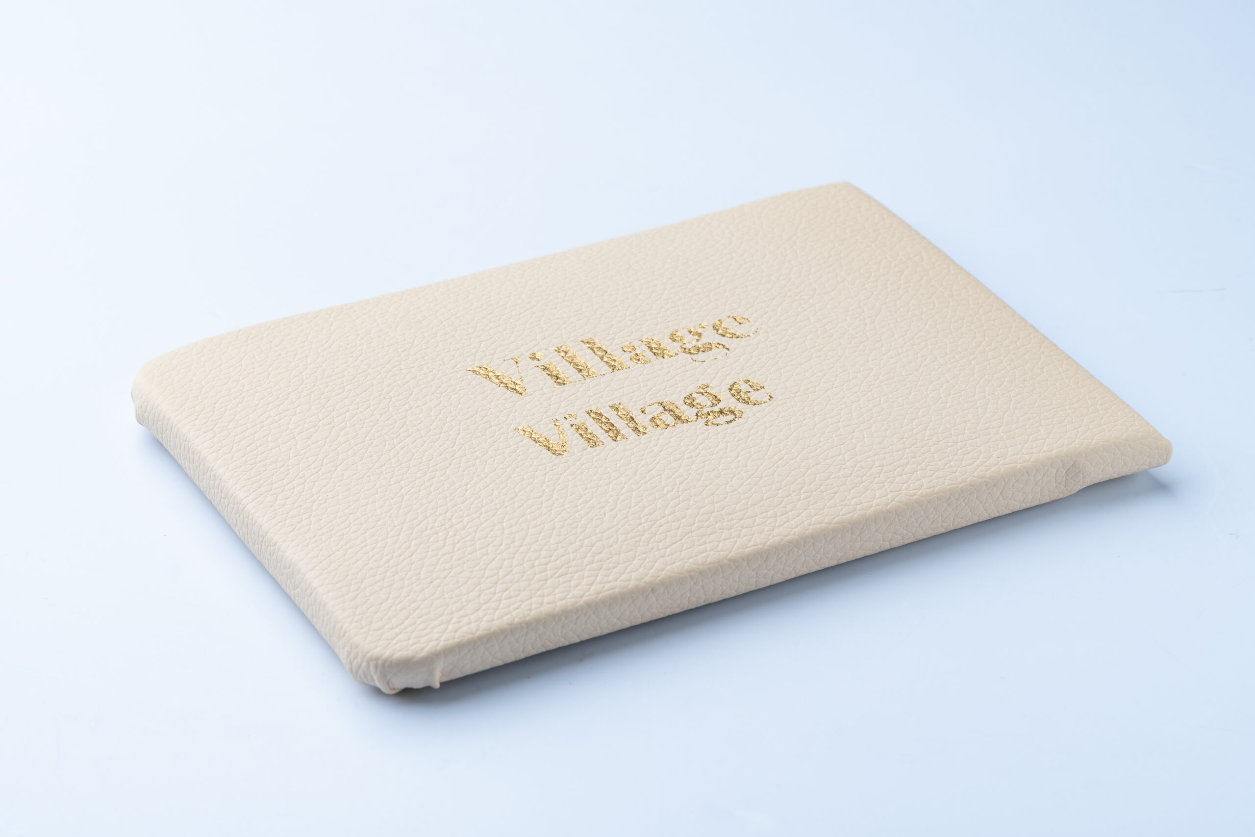Cream-colored notebook with 'Village Village' embossed on cover on light blue background.